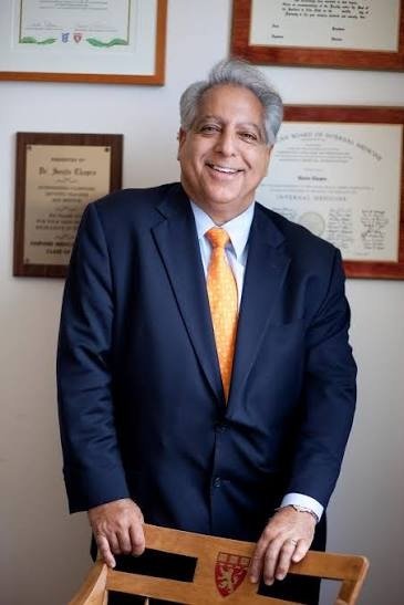 Dr. Sanjiv Chopra smiling in a navy suit and gold tie